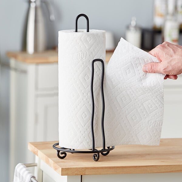 A hand holding a roll of paper towels on a black wire paper towel holder.