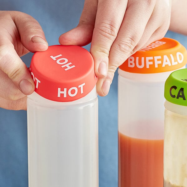 A person using a white Choice "Hot" silicone lid to cover a bottle of hot sauce.