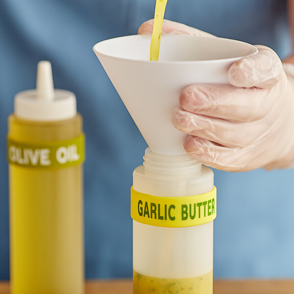 A hand pouring garlic butter into a squeeze bottle using a funnel.