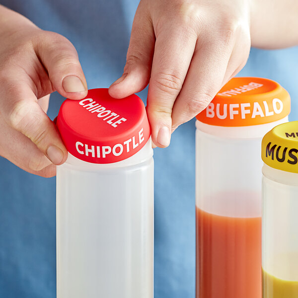 A person using a Choice Chipotle silicone lid to dispense orange liquid from a squeeze bottle.