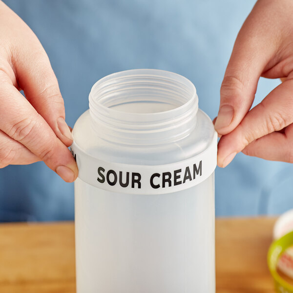 A person's hand using a "Sour Cream" label band on a silicone squeeze bottle.