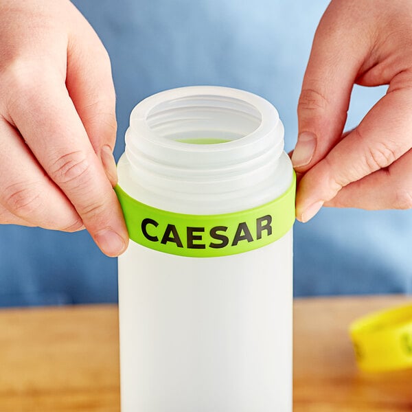 A person's hand squeezing a bottle with a white silicone label that reads "Caesar"