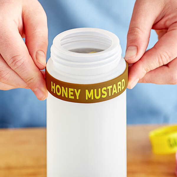 A person holding a small bottle with a Honey Mustard label band.