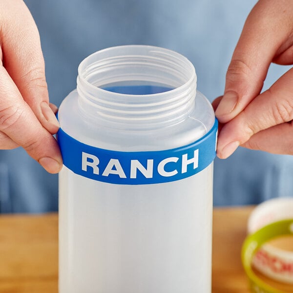 A person holding a plastic bottle with a green and white "Ranch" label band around the lid.
