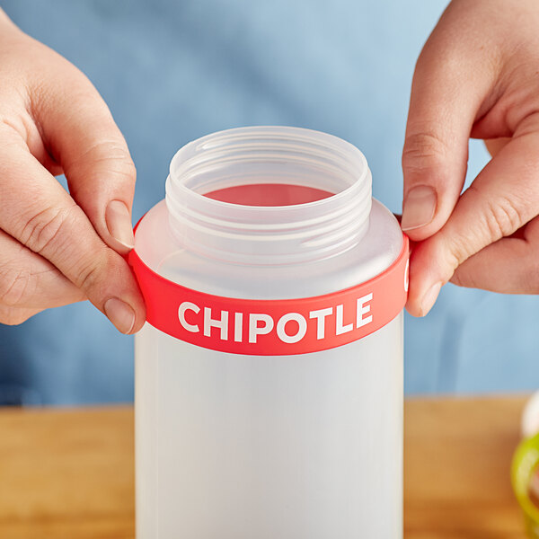A person's hand squeezing a silicone label band onto a plastic bottle with "Chipotle" on it.