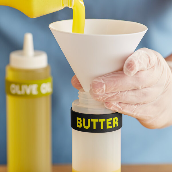 A hand pouring butter from a yellow container into a plastic squeeze bottle.