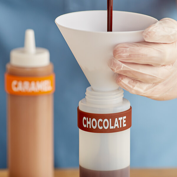 A gloved hand using a Chocolate Silicone Squeeze Bottle to pour chocolate into a container.