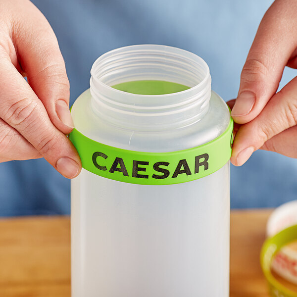 A person holding a plastic container with a green "Caesar" label band around the lid.