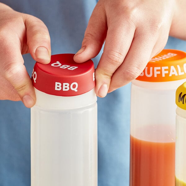 A person's hand using a red "BBQ" silicone lid to cover a squeeze bottle of sauce.