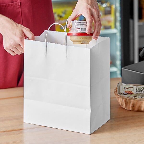 A person putting a jar of food into a white paper bag.