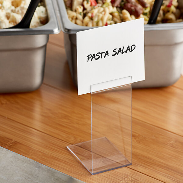 A clear plastic Choice deli tag holder on a table in front of a bowl of pasta.