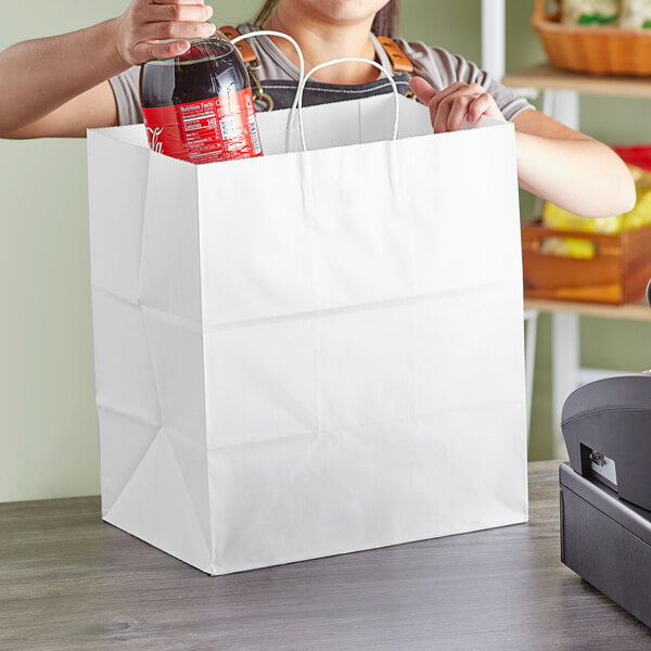 A person holding a white bag with a bottle of soda inside.