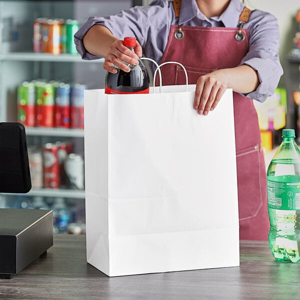 A woman putting a bottle of soda into a white paper shopping bag.