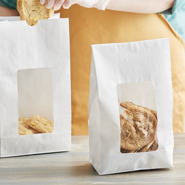 A woman putting a cookie into a white paper bag with a window.