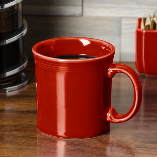 A red Fiesta java mug on a wood table with coffee in it.