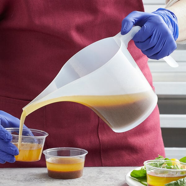 A person in blue gloves pouring yellow liquid into a Fox Run translucent measuring cup.