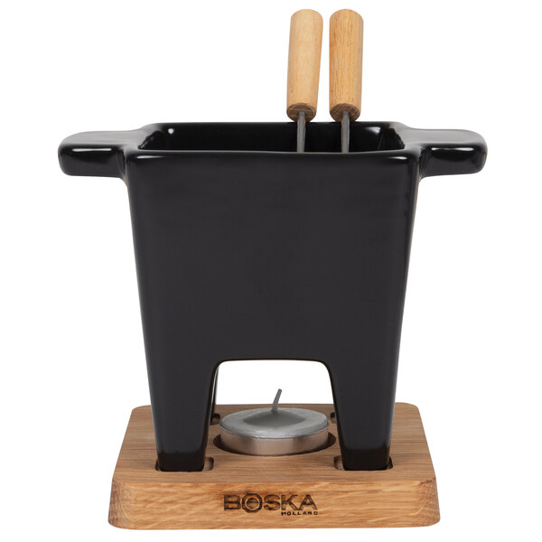 A black ceramic Boska tapas fondue pot with wooden handles and two wooden sticks.