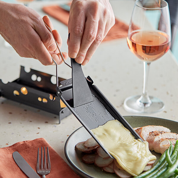A person using a knife to spread melted cheese on meat using a Boska Milano Partyclette.