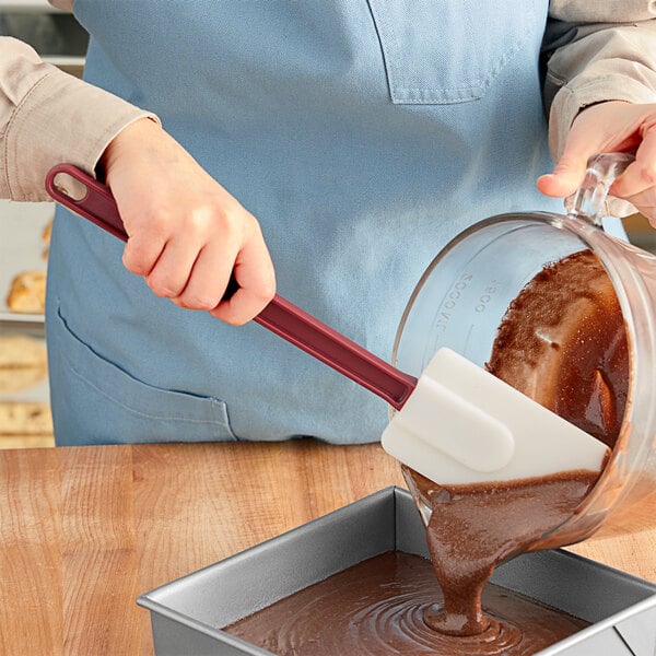 A person using a Choice 14" Heat-Resistant Silicone Spatula to pour chocolate into a pan.