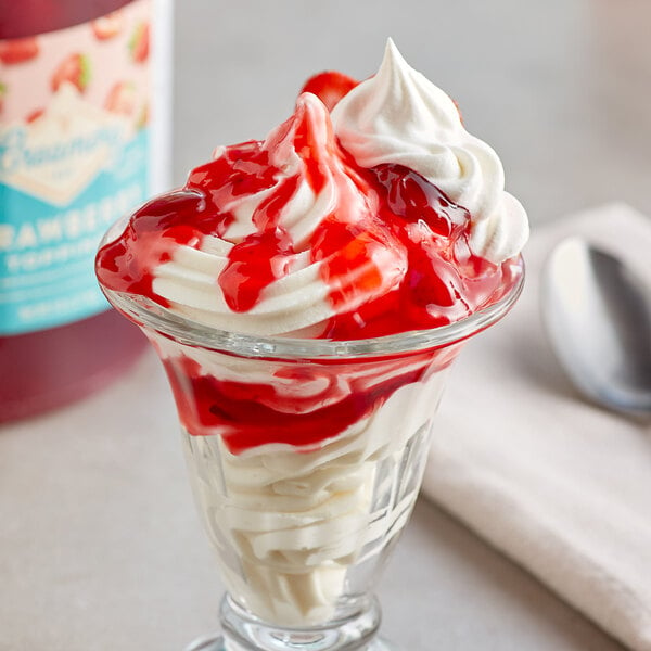 A glass cup of strawberry ice cream with whipped cream and red syrup.