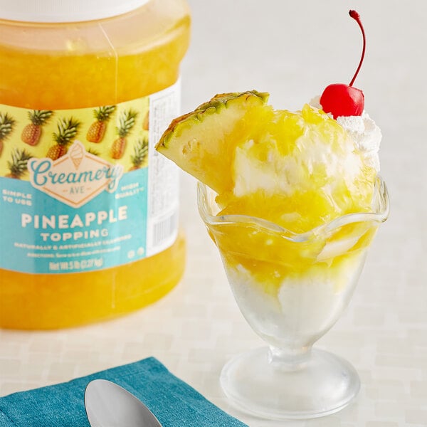 A glass with a yellow and white dessert topped with Creamery Ave. Pineapple Dessert next to a jar of Creamery Ave. Pineapple Topping.