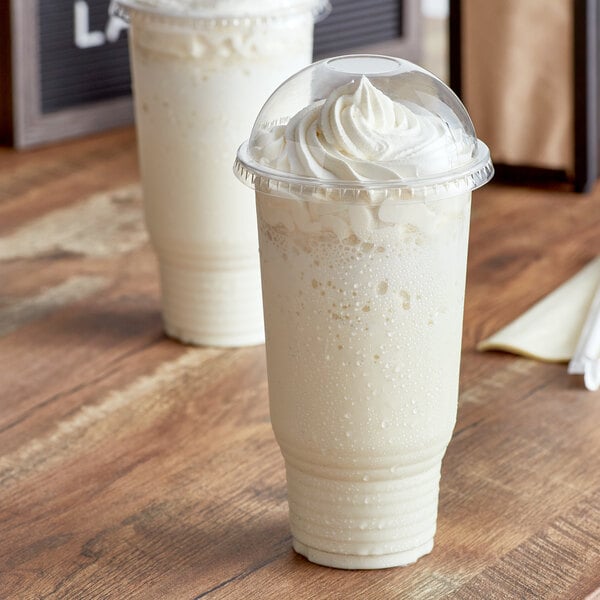 Two Choice clear plastic cups of milkshake with whipped cream on top.