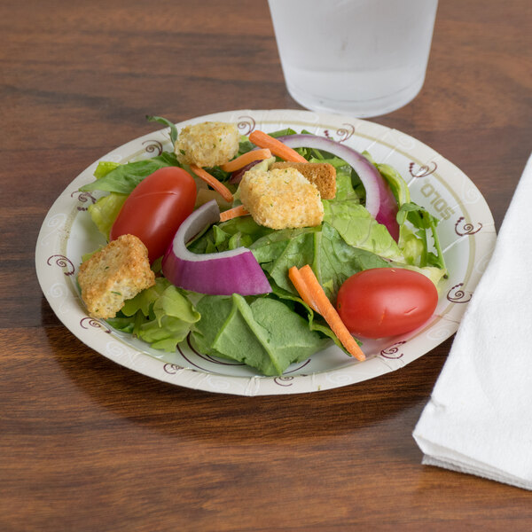 A Solo Symphony heavy weight paper plate with a salad with croutons and tomatoes on it with a glass of water and a napkin.