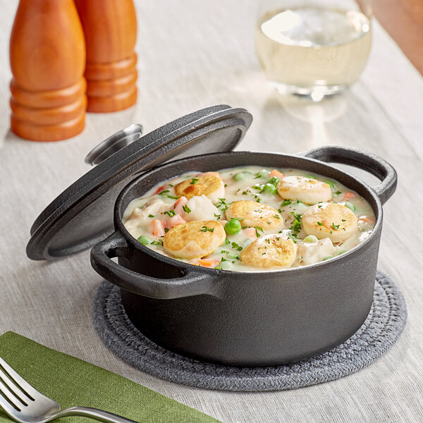 A Valor pre-seasoned mini cast iron dutch oven filled with soup, meat, and vegetables with a lid on a green surface.