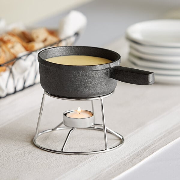 A Valor pre-seasoned mini cast iron fondue pot with stand over a candle