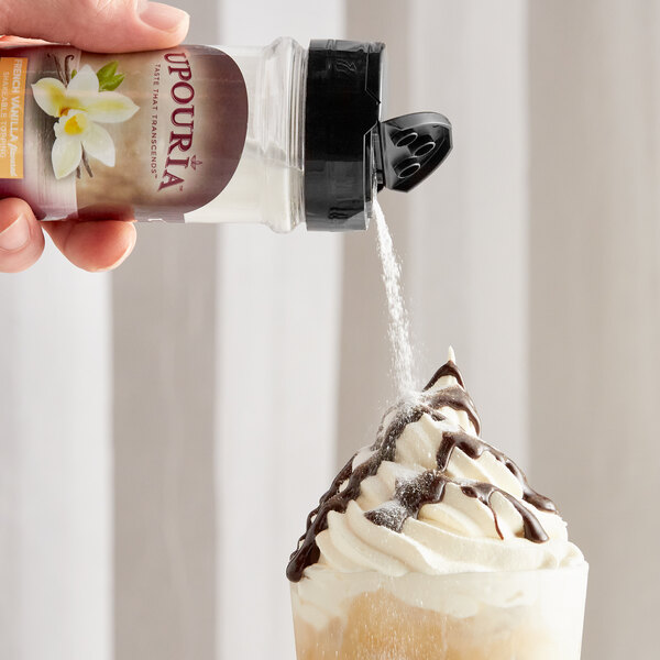 A hand pouring UPOURIA French Vanilla powder onto a drink with whipped cream.