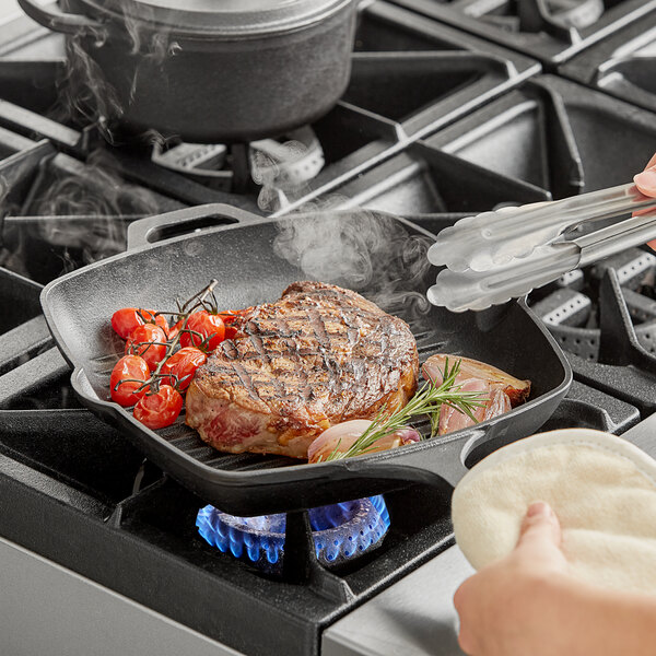 A person using a Valor square cast iron grill pan to cook a steak on a stove.