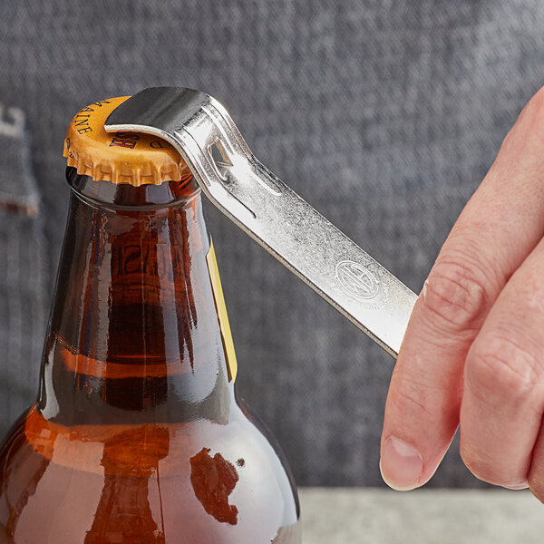 A hand using an American Metalcraft stainless steel bottle opener to open a beer bottle with a cap.
