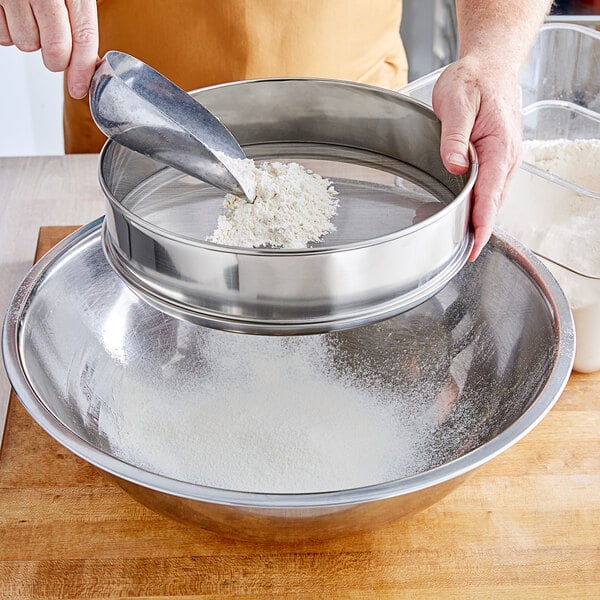 A person using a Choice stainless steel sieve to sift white powder into a bowl.