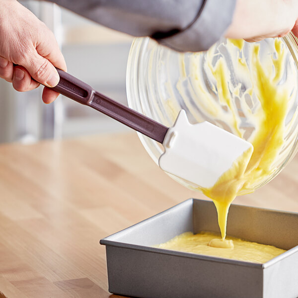 A person using a Mercer Culinary Hell's Tools high temperature silicone spatula to pour yellow liquid into a pan.