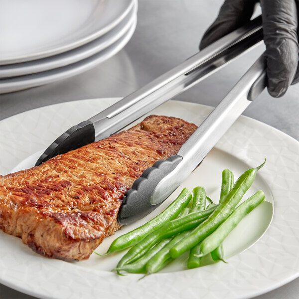 A person using OXO Good Grips tongs to serve steak with green beans on a plate.