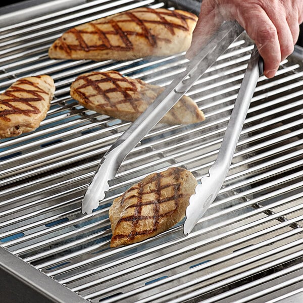 A person using OXO stainless steel grilling tongs to cook meat on a grill.