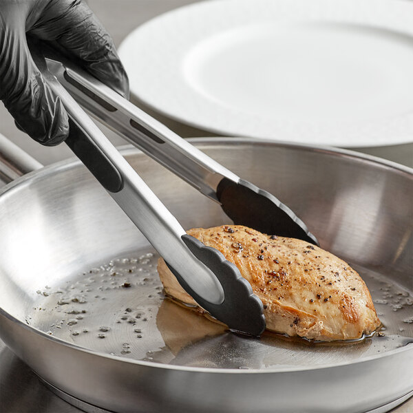 A person using OXO tongs to hold a piece of meat in a pan.