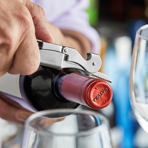 A person using an Acopa Waiter's Corkscrew to open a bottle of wine at a table in an Italian restaurant.