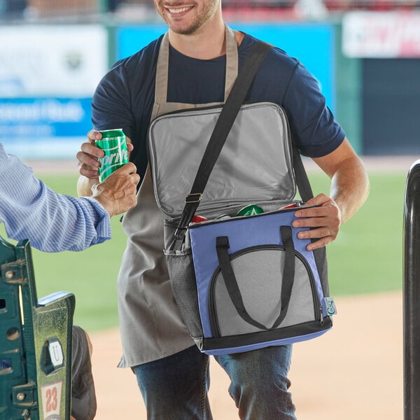 A man opening a Choice navy insulated cooler bag full of cans on a baseball field.