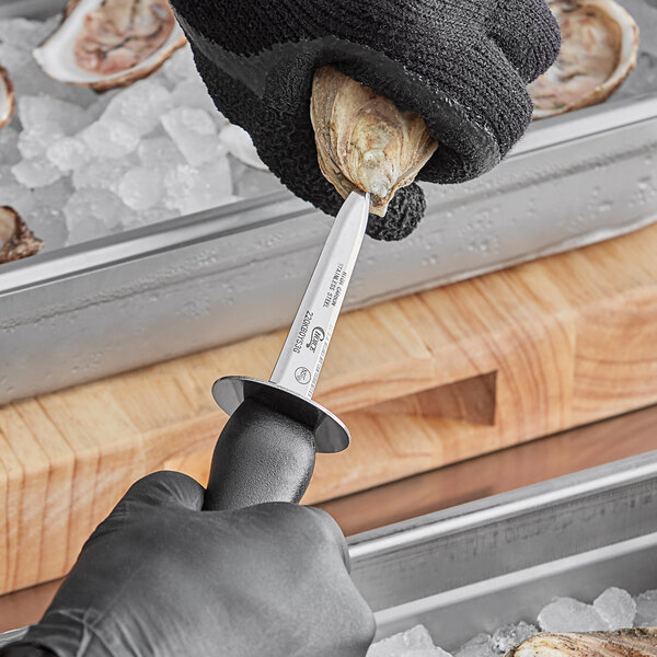 A person in a black glove using a Choice Boston Style Oyster Knife with a black hourglass handle to open an oyster shell.