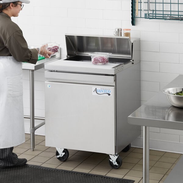 A woman in a white apron using an Avantco commercial sandwich and salad prep refrigerator.