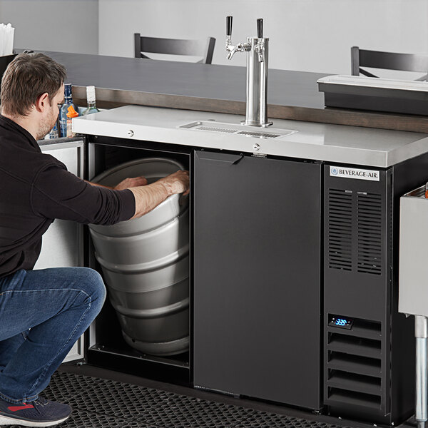 A man in a black shirt and jeans using a Beverage-Air wine kegerator to open a keg.