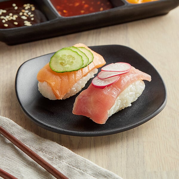 A plate of sushi with cucumber, salmon, and ginger on a black matte square melamine plate.