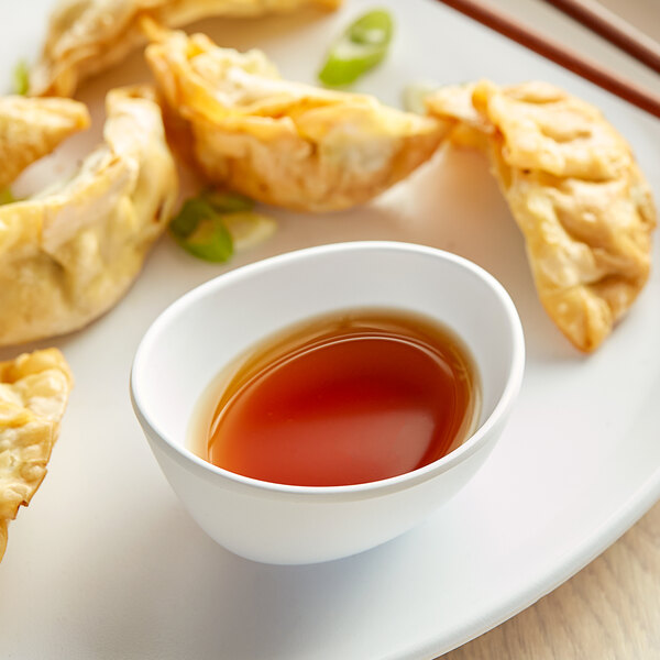 A white plate of fried dumplings with a white irregular round matte melamine ramekin of brown sauce.
