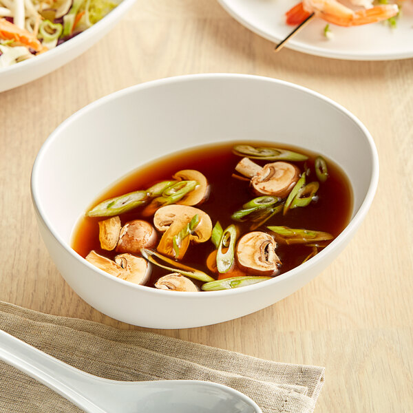 A white GET Enterprises Riverstone melamine bowl filled with soup containing mushrooms and green onions.