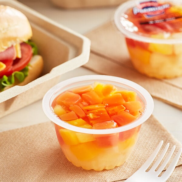 A plastic container of Premium Tropical Fruit Mix on a table with a sandwich.