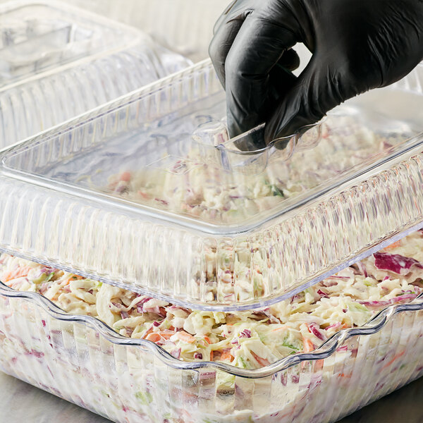 A person wearing black gloves using a clear plastic container to serve salad at a salad bar.