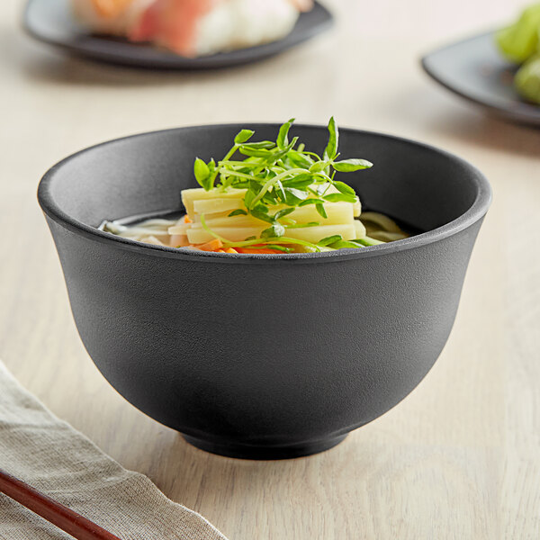 A black matte melamine bowl filled with soup, vegetables, and herbs.