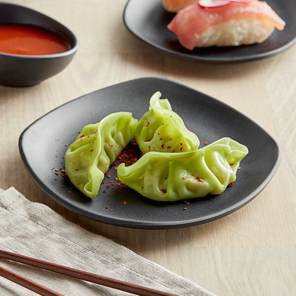 A GET Nara black matte square melamine plate with two dumplings and chopsticks next to a bowl of red sauce on a table.