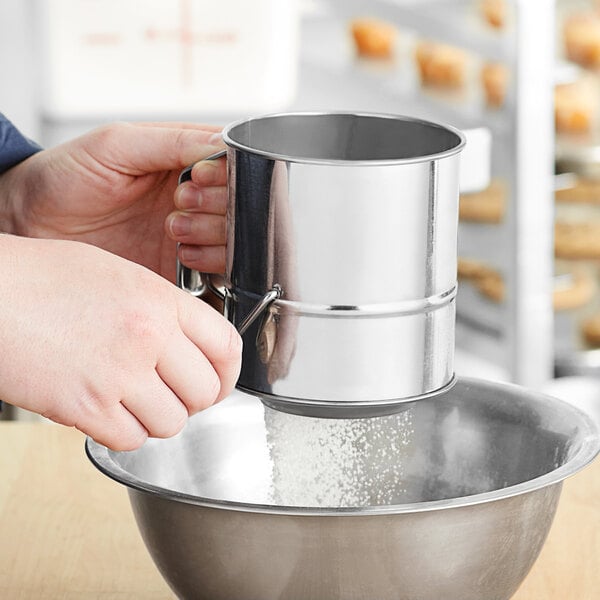 A person using a Fox Run stainless steel sifter to pour powdered sugar into a bowl.